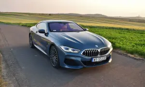 Niebieskie BMW 840d na tle pól zbożowych o zachodzie słońca.