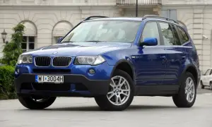 Niebieskie BMW X3 2005 z polskimi tablicami rejestracyjnymi WI 3004H zaparkowane przed budynkiem.