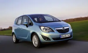 Niebieski Opel Meriva 1.4 benzyna w ruchu, z kierowcą za kierownicą, na tle zielonych pól i drzew.