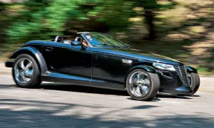 Czarny Plymouth Prowler z opuszczonym dachem pędzi po krętej drodze, otoczony rozmazaną zielenią drzew.