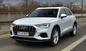 Białe Audi Q3 w ruchu drogowym. Kierowca za kierownicą. Wiele osób szuka audi q3 opinie przed zakupem.