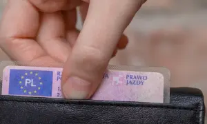 Dłoń wkłada do portfela polskie prawo jazdy. Dokument jest bezterminowe, co oznacza swobodę na drogach.