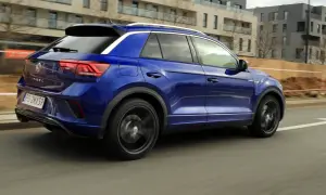 Niebieski Volkswagen T-Roc pędzi ulicą. W tle nowoczesne budynki i plac budowy.