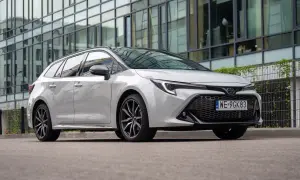 Biała Toyota Corolla 2.0 Hybrid na tle nowoczesnego budynku.