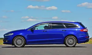 Niebieski kombi Ford Mondeo na tle błękitnego nieba z chmurami. Kierowca w czapce z daszkiem za kierownicą.