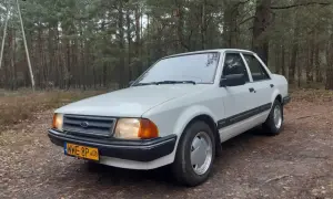 Biały Ford Orion z lat 80. stoi na leśnej drodze.