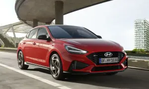 Czerwony Hyundai i30 hatchback N Line w ruchu miejskim, z nowoczesną architekturą w tle.