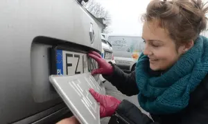 Kobieta w czerwonych rękawiczkach montuje tablicę rejestracyjną. To ważny etap lch rejestracja pojazdu.