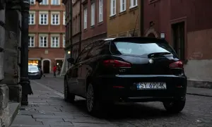 Czarny Alfa Romeo 147 na wąskiej uliczce. Czyj to numer rejestracyjny samochodu? SY 6904K.