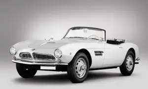 Biały kabriolet BMW 507 z lat 50. prezentuje się elegancko na szarym tle.