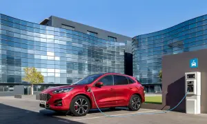 Czerwony Ford Kuga, nowoczesny kombi, ładuje się przy stacji ładowania przed futurystycznym budynkiem.