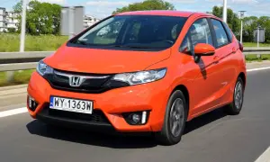 Pomarańczowy Honda Jazz w ruchu drogowym. Wiele osób szuka honda jazz opinie przed zakupem.