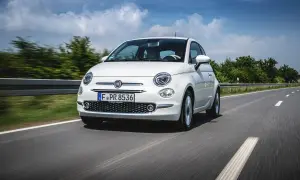 Biały fiat mini pędzi po asfaltowej drodze, otoczony zielenią i błękitnym niebem z chmurami.