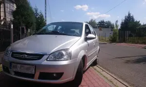 Srebrny tata indica zaparkowany przy czerwonym chodniku. W tle dom i drzewa.