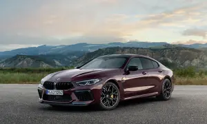 Eleganckie BMW M8 w kolorze głębokiej wiśni, zaparkowane na tle malowniczych, pofałdowanych wzgórz o zachodzie słońca.