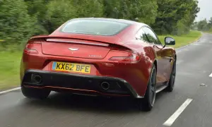 Czerwony Aston Martin Vanquish pędzi po mokrej drodze, otoczony zielenią.