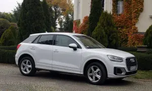 Białe Audi Q2 na brukowanym podjeździe, otoczone zielenią i jesiennymi liśćmi. Idealne do miasta, jak sugerują pierwsze audi q2 opinie.