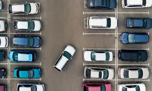 Widok z góry na parking z wieloma samochodami zaparkowanymi prostopadle. Jeden biały samochód jest zaparkowany pod kątem.