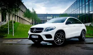 Biały Mercedes GLE 450 zaparkowany na mokrym asfalcie przed nowoczesnym budynkiem.