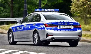 Srebrny radiowóz policyjny z niebieskimi pasami i napisem "POLICJA" na drzwiach i tyle. Widoczna tablica rejestracyjna HPZ C341.