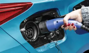 Dłoń z czerwonym lakierem na paznokciach podłącza ładowarkę do niebieskiej hybrydy plug-in.