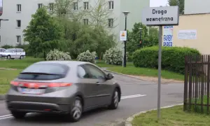 Znak "Droga wewnętrzna" informuje o zasadach ruchu na tym terenie. Samochód w ruchu.