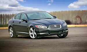 Czarny Jaguar XF na torze. Kierowca w środku, chmury na niebie. Wiele pozytywnych jaguar xf opinie potwierdza jego sportowy charakter.