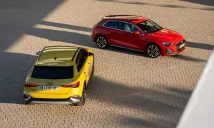 Dwa Audi A3 kombi, żółte i czerwone, zaparkowane na brukowanym placu, oświetlone słońcem i cieniami.