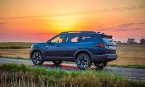 Ciemnoniebieska Dacia 4x4 na tle zachodzącego słońca, na polnej drodze.