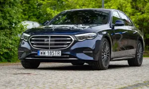 Elegancki, ciemnogranatowy Mercedes e300 lśni po deszczu na tle zieleni.