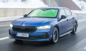 Niebieska Skoda Superb 2.0 TSI pędzi po mokrej drodze, tworząc wrażenie prędkości.