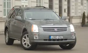 Szary Cadillac SRX z tablicą rejestracyjną JXE-252 zaparkowany przed budynkiem.