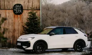 Biały, mały SUV zaparkowany obok drewnianej chaty z napisem "Polna Hill SPA" i choinką ozdobioną lampkami.