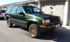 Zielony Jeep Grand Cherokee Limited z lat 90. na złotych felgach, zaparkowany przed garażami.