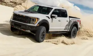 Biały Ford F-150 Raptor szaleje po piaszczystych wydmach, wzbijając tumany piasku.