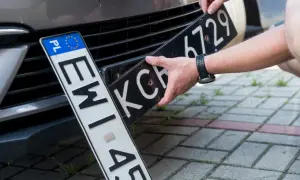 Ręce montują tablicę rejestracyjną do samochodu. Nowa elc rejestracja czeka na zamontowanie.