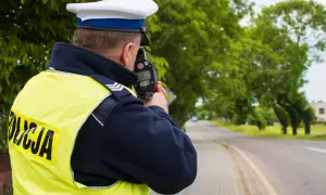 Policjant w kamizelce odblaskowej mierzy prędkość samochodu za pomocą fotoradaru.