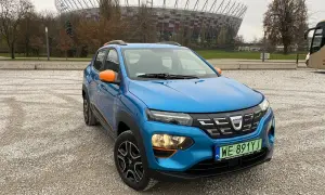 Niebieska Dacia Spring z pomarańczowymi akcentami na tle Stadionu Narodowego. Dacia Spring opinie – miejski elektryk gotowy na przygodę.