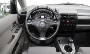Wnętrze Audi A2 z kierownicą, deską rozdzielczą i dźwignią zmiany biegów. Widoczne wskaźniki, radio i przyciski.