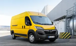 Żółty Opel Movano stoi na parkingu przed nowoczesnym budynkiem przemysłowym.