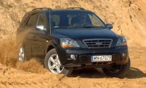 Czarny Kia Sorento 1. pokonuje piaszczysty teren, wzbijając tumany kurzu.