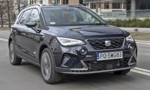 Ciemnoniebieski Seat Arona w ruchu ulicznym. Kierowca w okularach. Wiele pozytywnych seat arona opinie potwierdza jego miejski charakter.