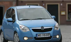 Niebieski Opel Agila 1.2 na brukowanej ulicy przed budynkiem.