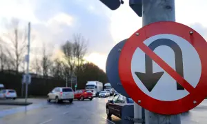 Znak zakazu zawracania na skrzyżowaniu. Samochody stoją w deszczu, czekając na zielone światło.