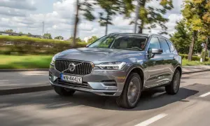 Szary Volvo XC60 T8 w ruchu, z rozmytym tłem drzew i nieba.
