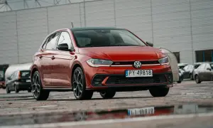 Czerwony Volkswagen Polo GTI z czarnym dachem, zaparkowany na mokrym parkingu.