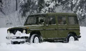 Zielony Mercedes G-klasa z napędem **awd** przebija się przez zaspy w zaśnieżonym lesie.