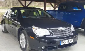 Czarny Chrysler Sebring pod wiatą, obok niebieski pickup.