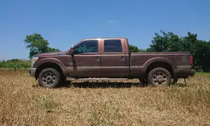 Brązowy Ford F250, ubrudzony ziemią, stoi na polu z suchą trawą.