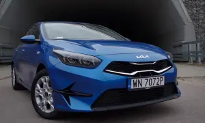 Niebieska Kia Ceed 1.5 T-GDI z nowoczesnymi światłami i grillem, zaparkowana przy betonowym tunelu.